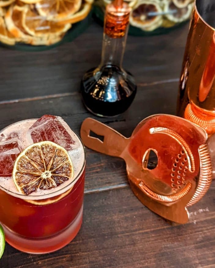 Copper Boston shaker, strainer, and jigger beside a finished cocktail