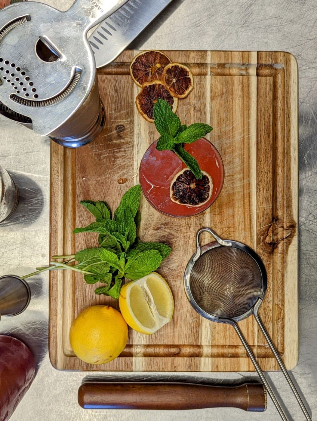 Prep board with cocktail, mint, citrus, and strainer laid out top-down